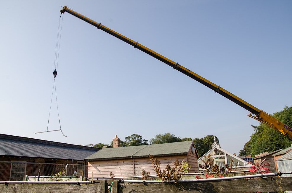 Crane lifting the first roof strut across the garden buildings and bothies to the conservatory